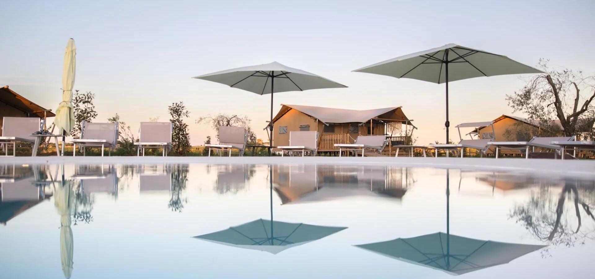 Piscina con lettini, ombrelloni e tende in un ambiente tranquillo e sereno.