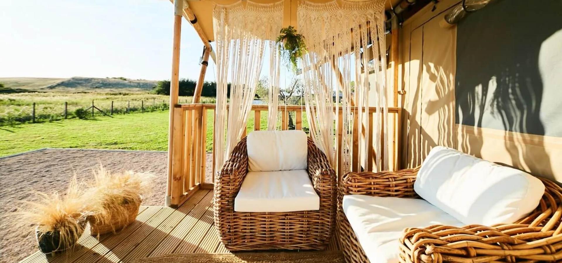 Veranda con sedie in vimini e tenda macramè, vista su prato verde.