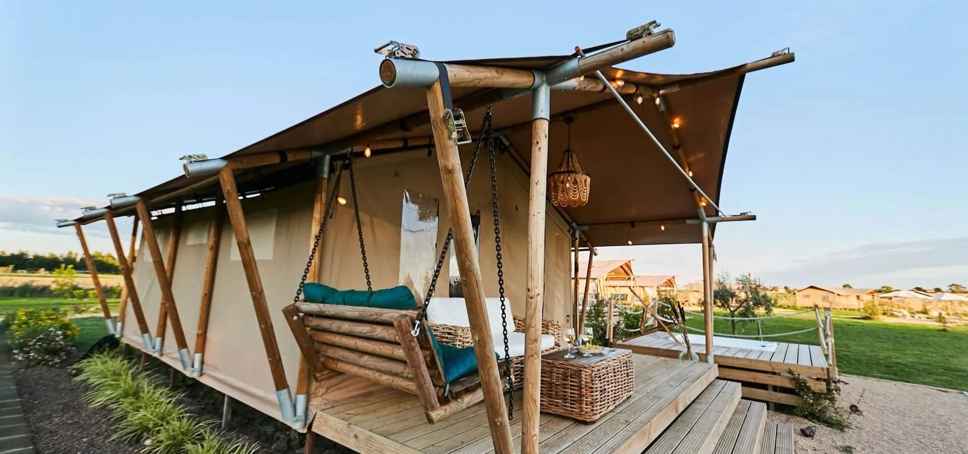 Tenda glamping con veranda, altalena e vista panoramica su un prato verde.
