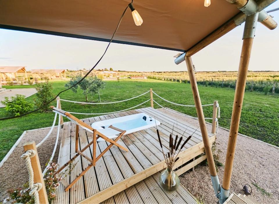 Terrazza in legno con vasca idromassaggio, immersa nel verde di un giardino.