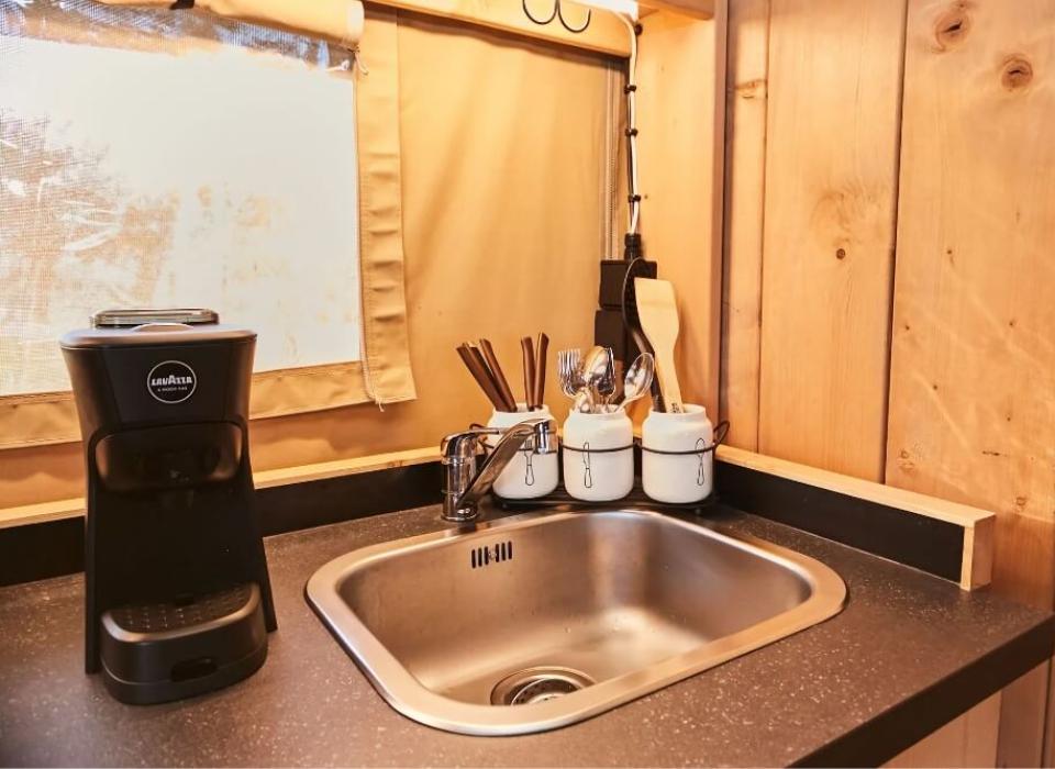 Angolo cucina con lavandino, macchina da caffè e utensili in contenitori bianchi.