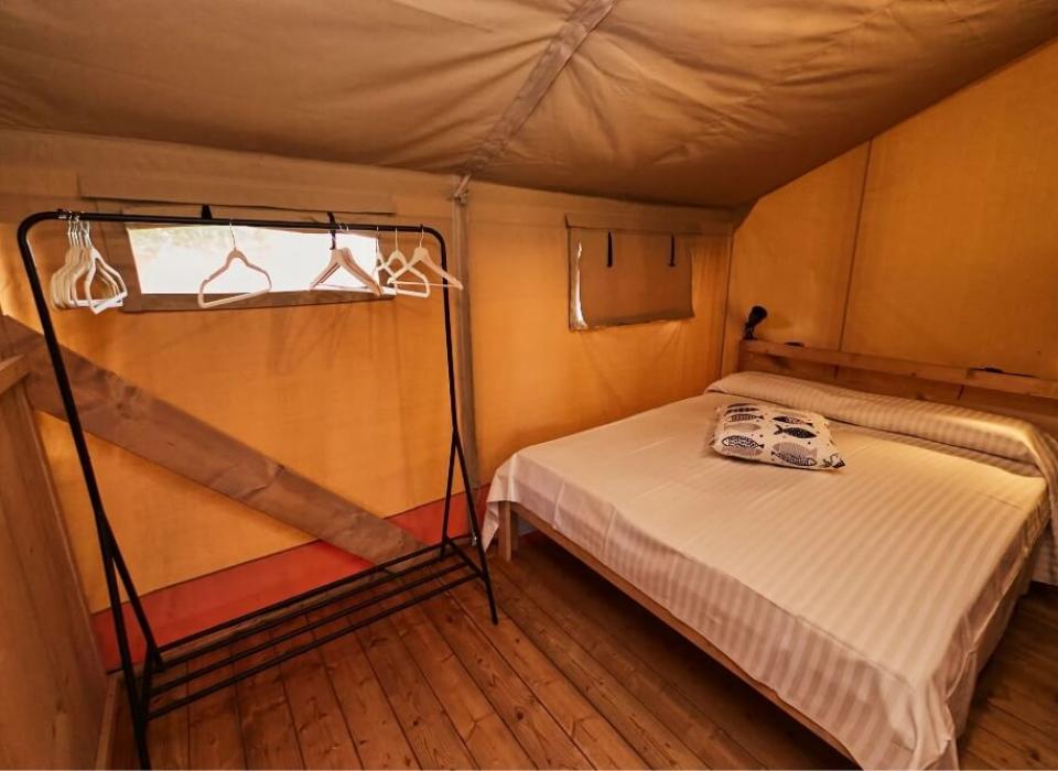 Interno di una tenda con letto matrimoniale e appendiabiti in metallo.