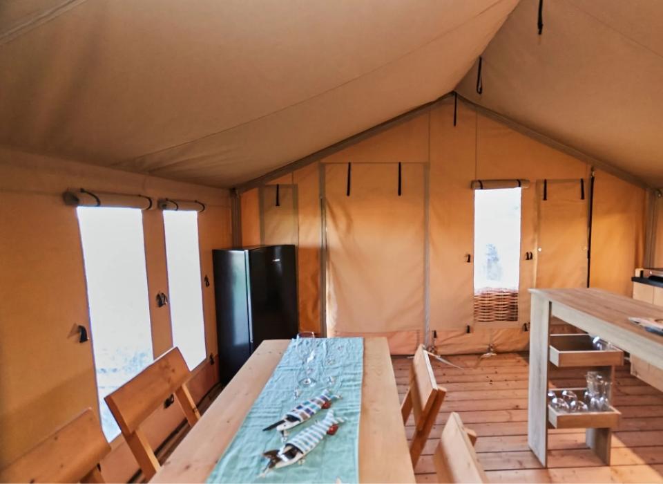Interno di una tenda glamping con tavolo, sedie e cucina attrezzata.
