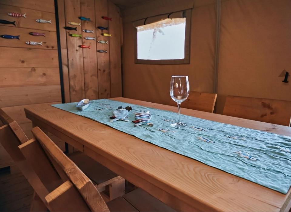 Interno rustico con tavolo in legno, decorazioni a pesci e bicchiere da vino.