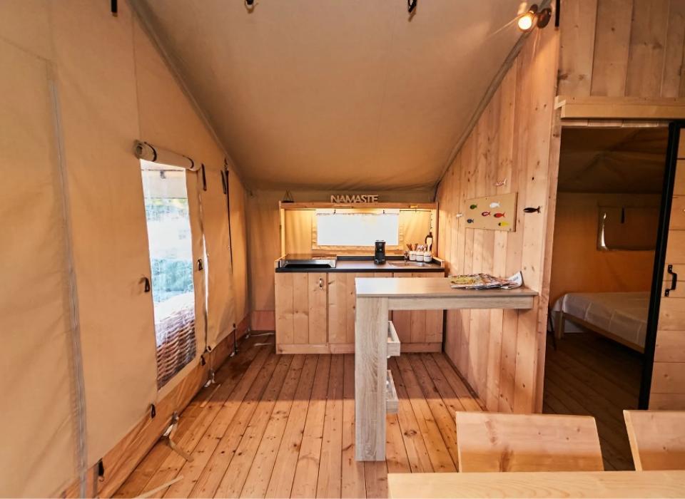 Interno di una tenda con cucina e area relax in legno.