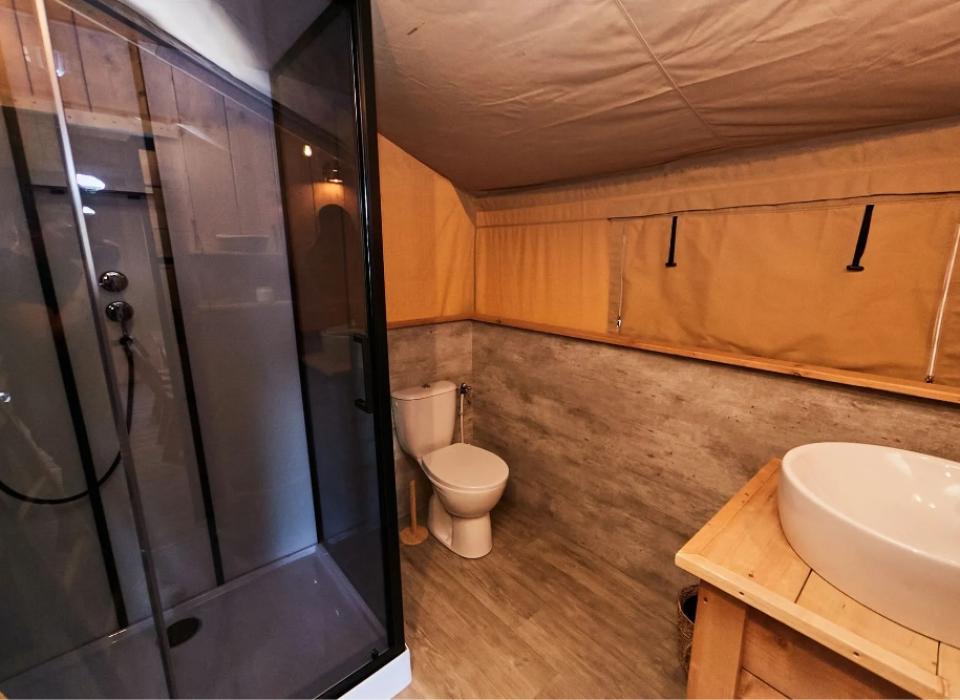 Bagno con doccia moderna, lavabo in legno e finestra con tendine beige.