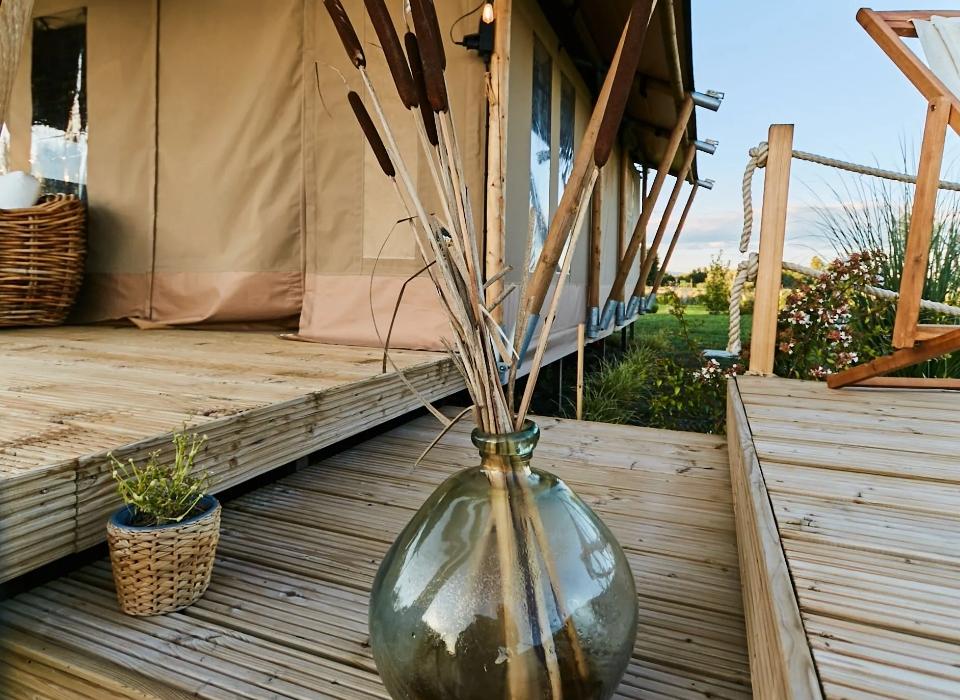Tenda glamping con decorazioni rustiche, vaso di vetro e piante su terrazza in legno.