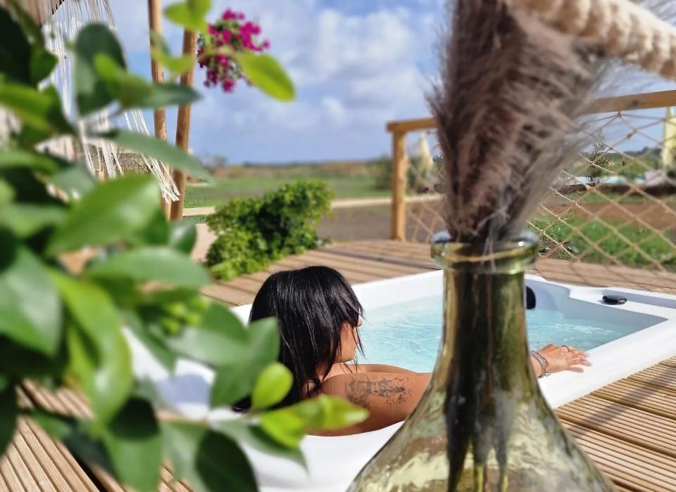 Donna in jacuzzi all'aperto, circondata da natura e decorazioni rustiche.