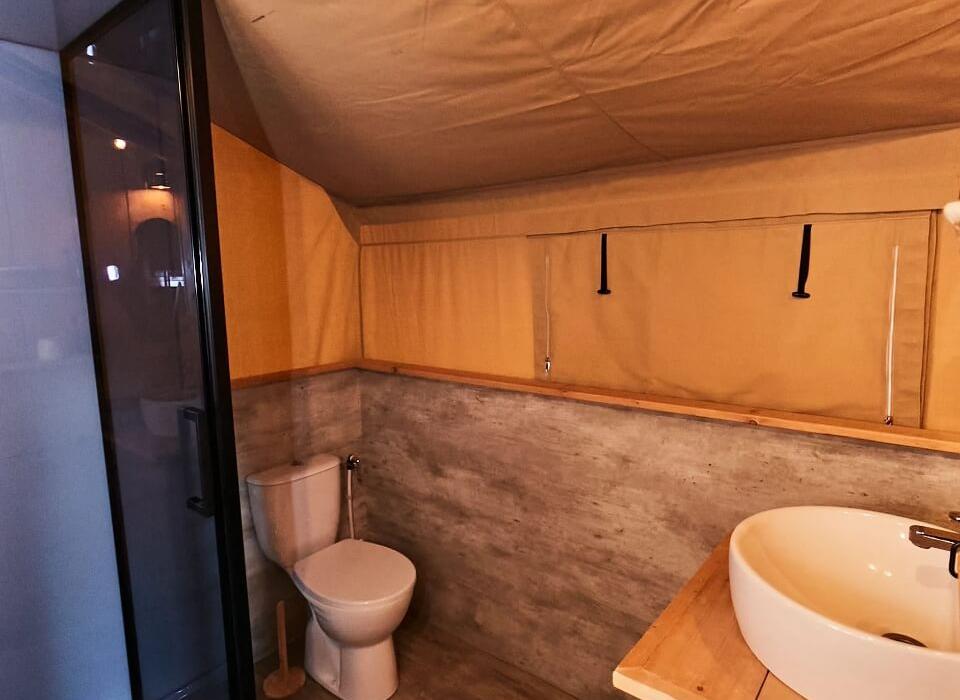 Bagno in una tenda, con doccia, lavandino e WC, stile rustico.