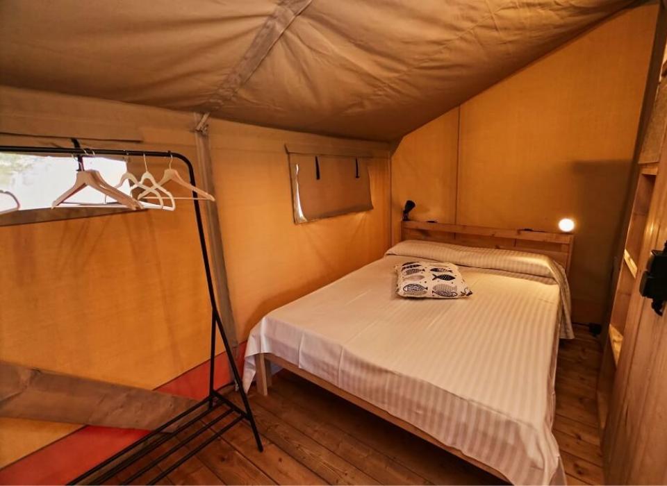 Interno di una tenda glamping con letto matrimoniale e appendiabiti.