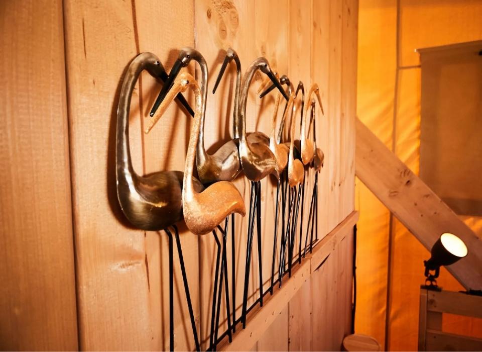 Sculture di uccelli metallici su parete di legno, illuminate da una luce calda.