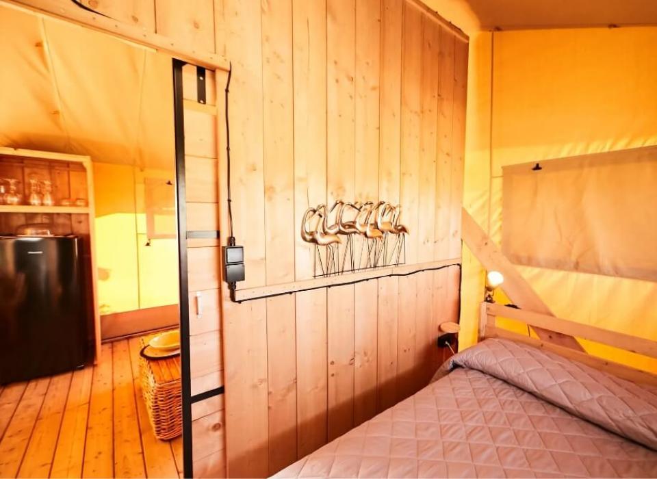 Interno di una tenda glamping con letto, frigorifero e decorazioni in legno.