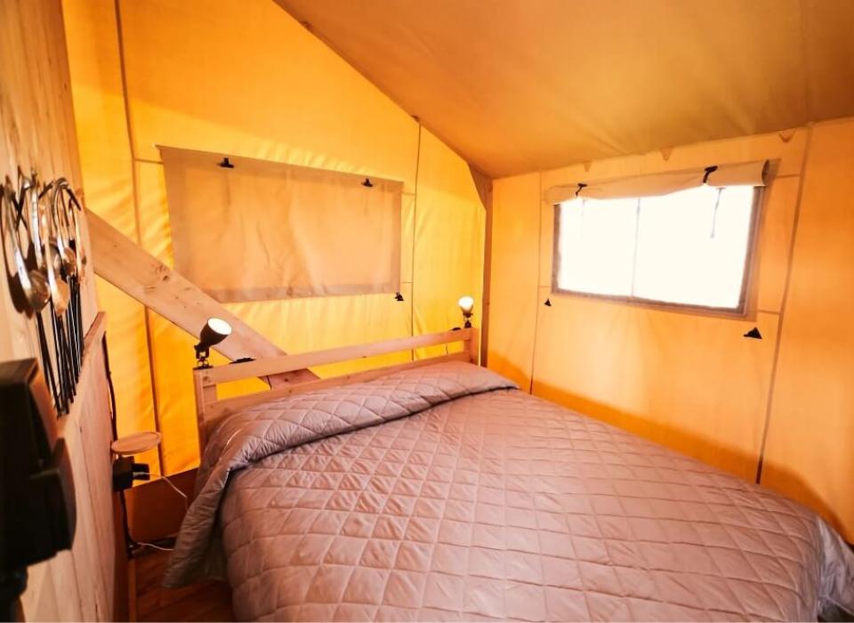 Camera da letto in tenda con letto matrimoniale e illuminazione accogliente.