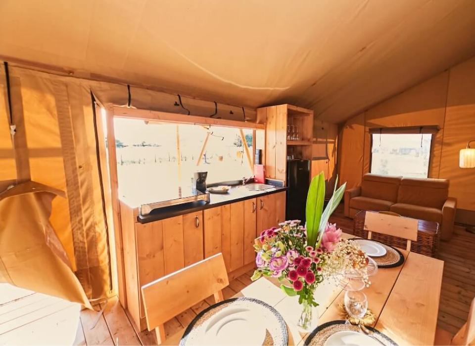 Interno di una tenda glamping con cucina, tavolo apparecchiato e divano.