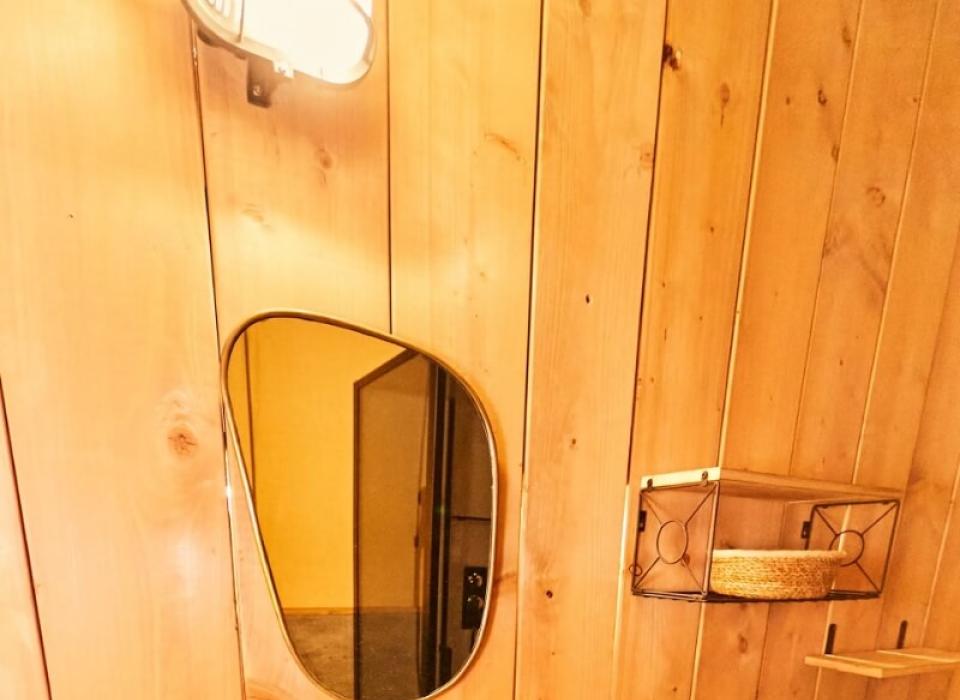 Bagno rustico con lavabo bianco, specchio ovale e mensole in legno.