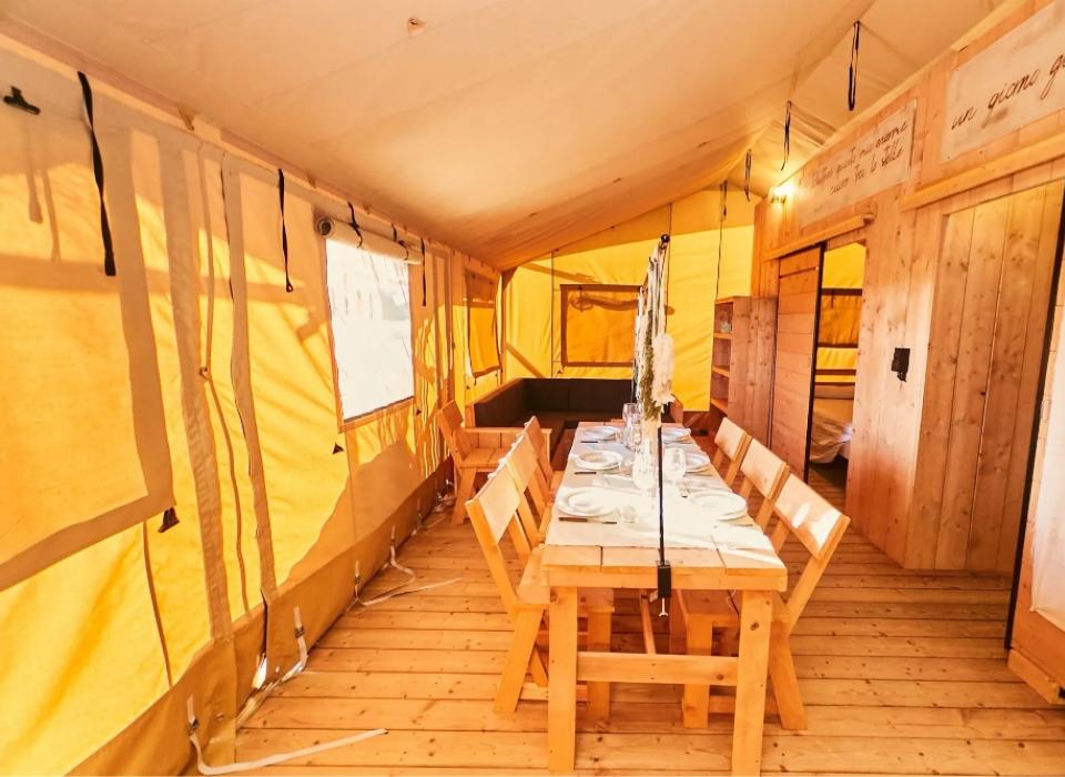 Interno di una tenda glamping con tavolo apparecchiato e arredamento in legno.