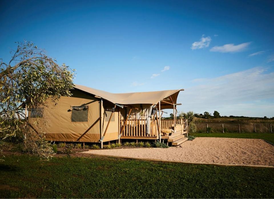 Tenda glamping in campagna, con veranda in legno e cielo sereno.