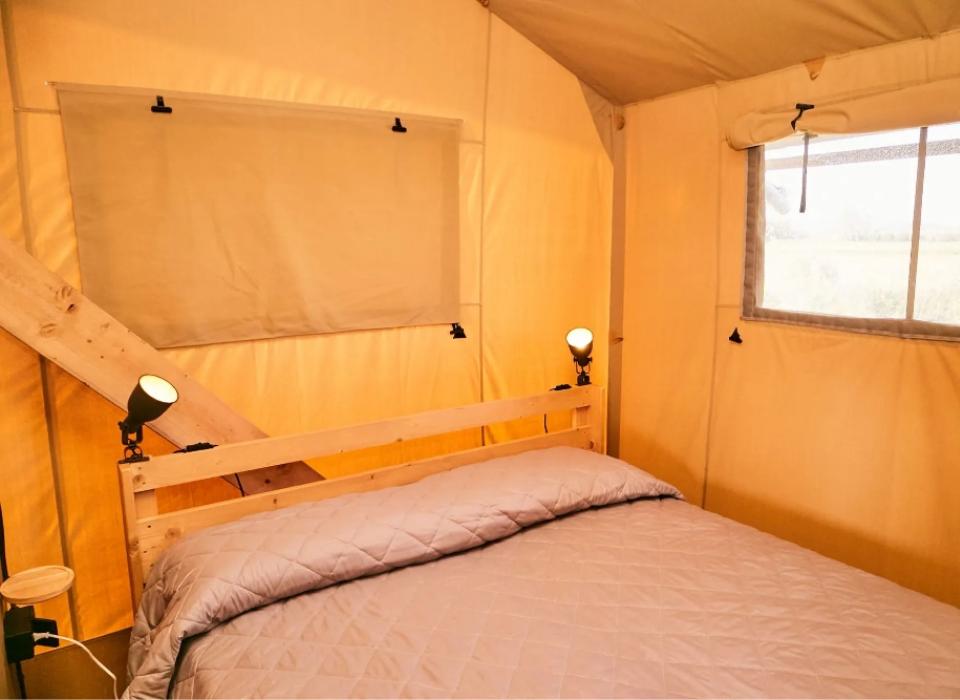 Interno di una tenda con letto matrimoniale e luci da lettura.