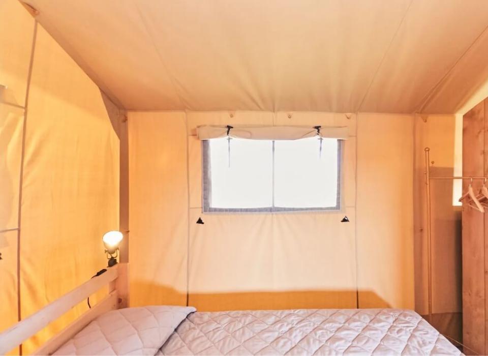 Interno di una tenda con letto e appendiabiti in legno, illuminazione calda.