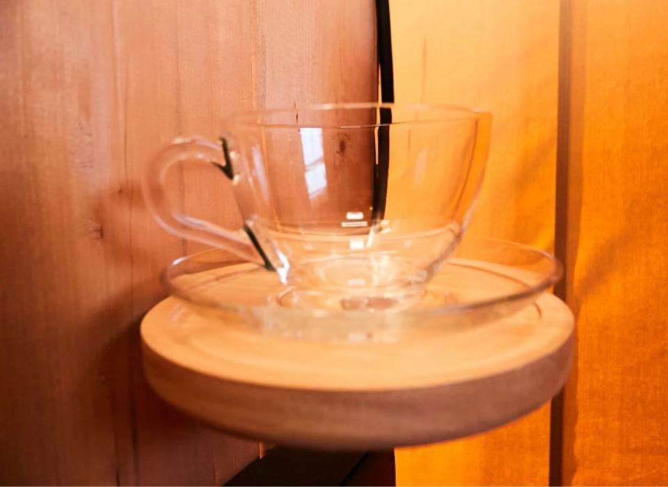 Tazza di vetro su piattino di legno, sfondo caldo e luminoso.