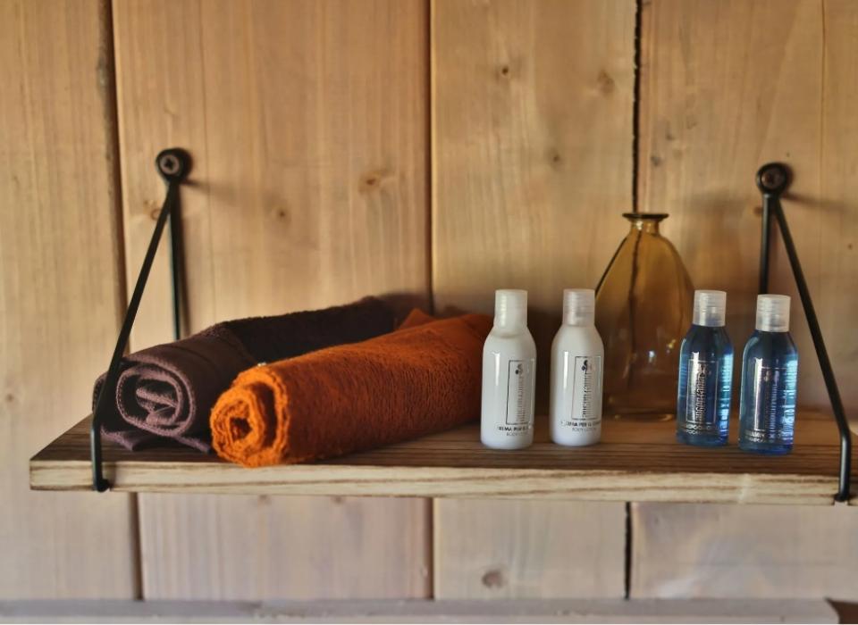 Mensola con asciugamani, flaconi di shampoo e crema, e un vaso decorativo.