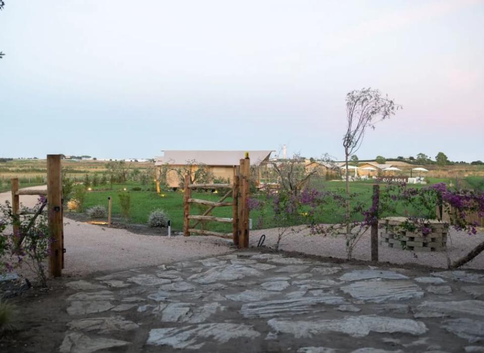 Ingresso rustico con giardino verde, sentiero e vista su edifici lontani.